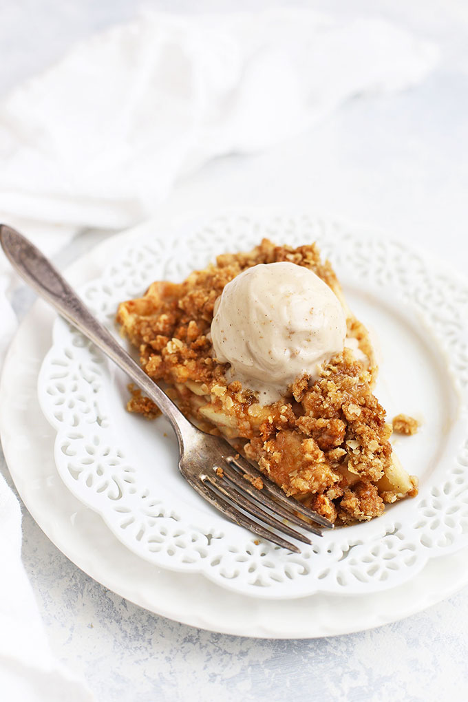 Front view of a slice of apple crumble pie with a scoop of vanilla ice cream melting on top. 