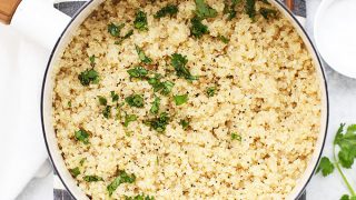 Overhead view of cooked quinoa in a saucepan with fresh herbs, salt and pepper