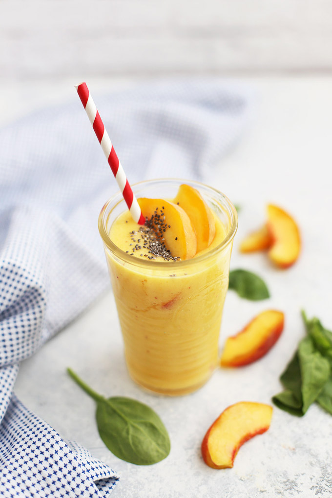 Front view of a glass of peach mango smoothie with fresh peach slices and chia seeds on top. 