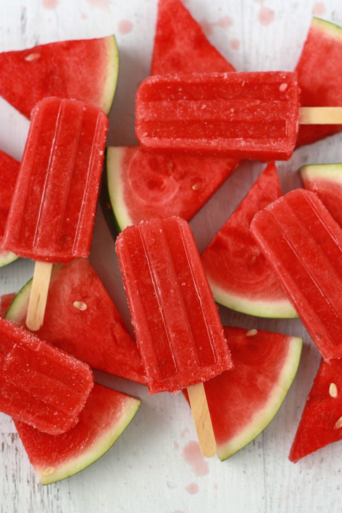 strawberry watermelon popsicles with wedges of fresh watermelon on a white background
