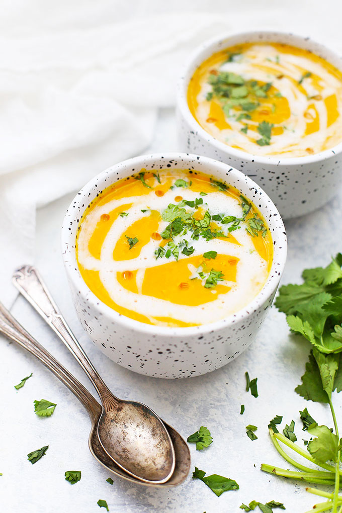 Front view of two bowls of curried butternut squash soup with coconut milk swirl and minced cilantro garnish