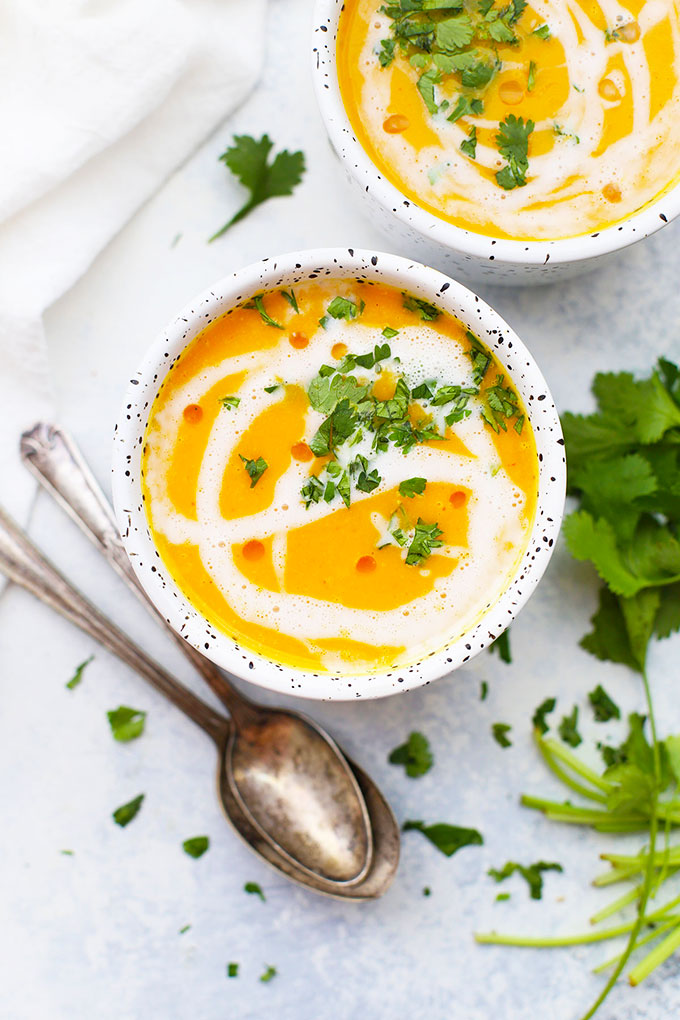 Close up view of 2 bowls of curry butternut squash soup with coconut milk swirl and cilantro garnish