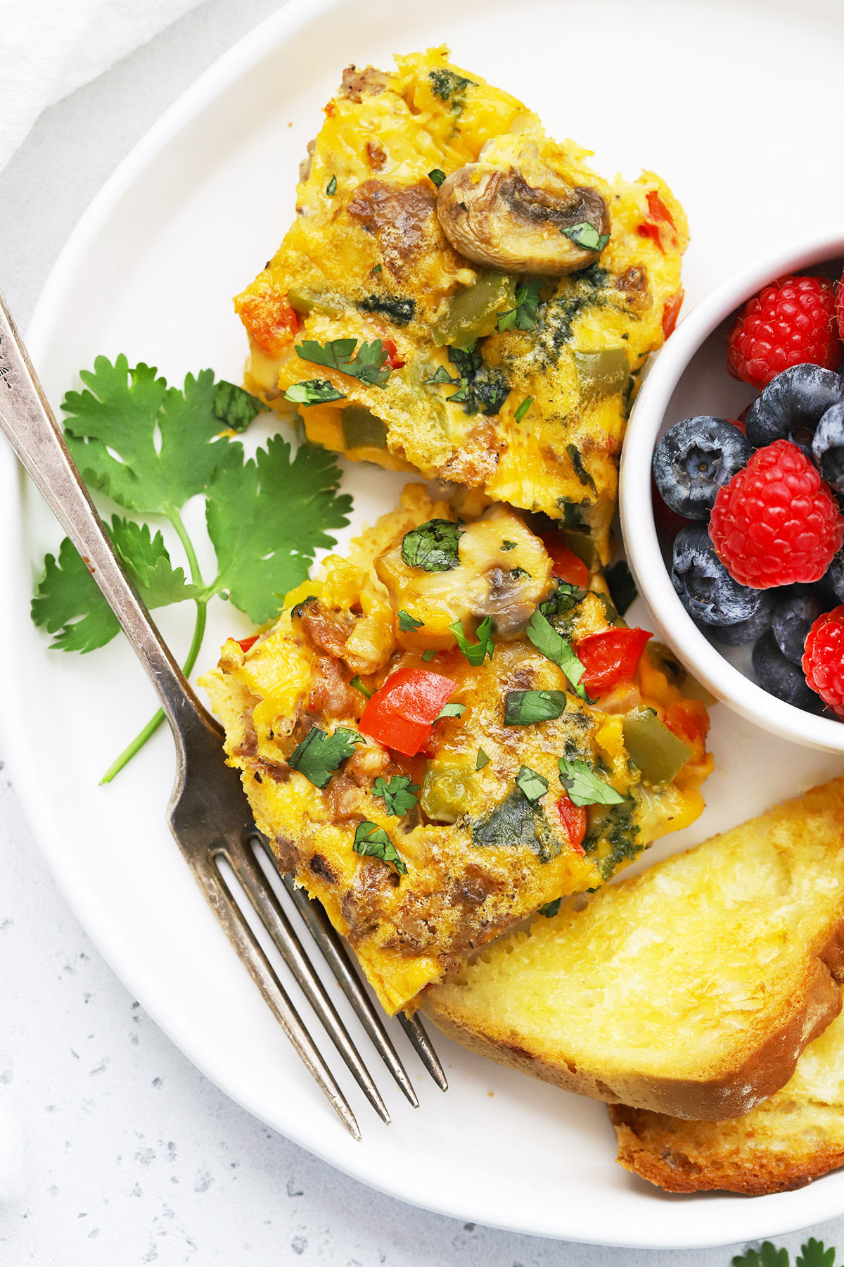 Close up view of slices of sausage and veggie breakfast bake on a plate with fresh berries + toast