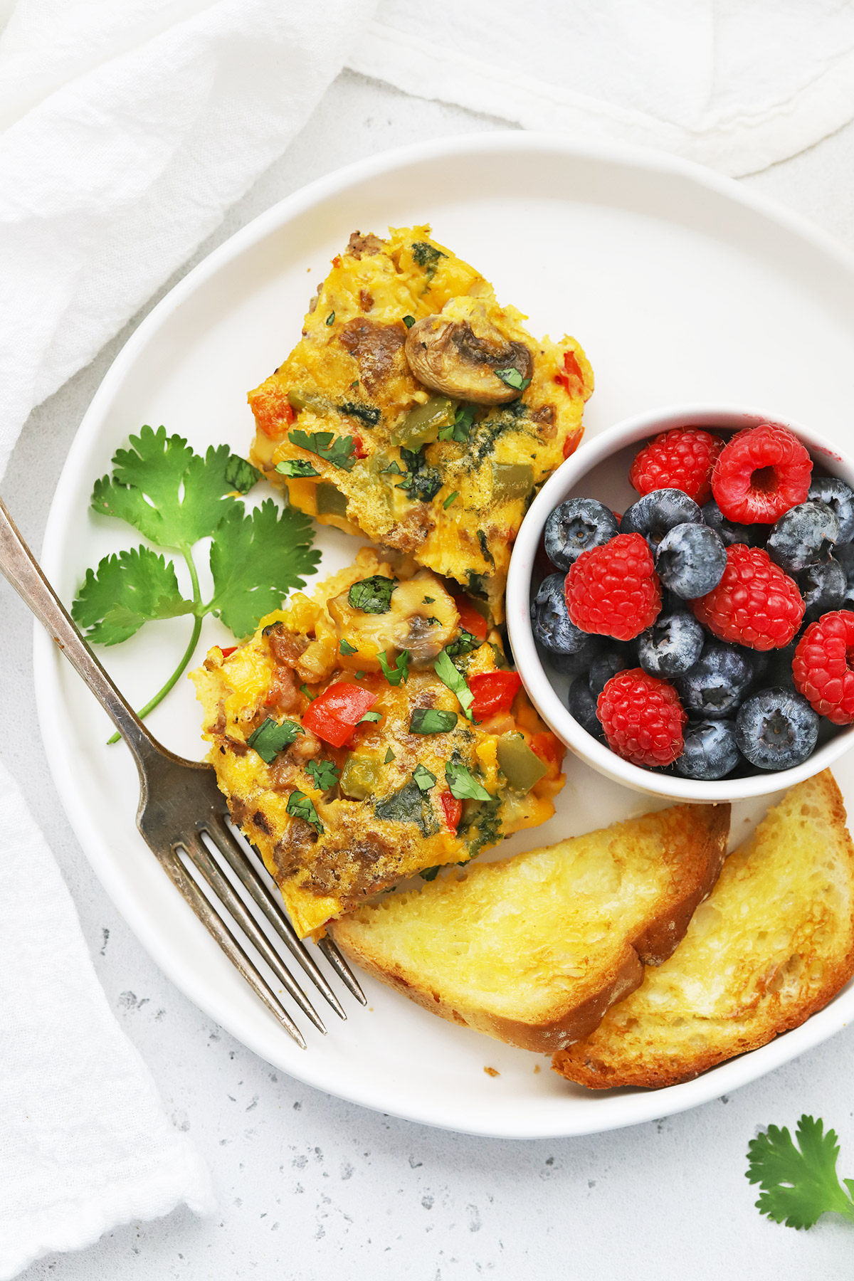slices of sausage and veggie breakfast bake on a plate with fresh berries + toast