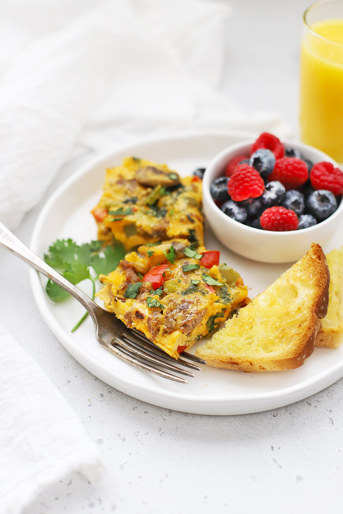 Front view of slices of sausage and veggie breakfast bake on a plate with fresh berries + toast