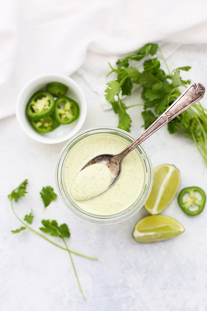 Tomatillo Ranch Dressing in a jar with a spoon. Jalapeño, lime, and cilantro garnish. 