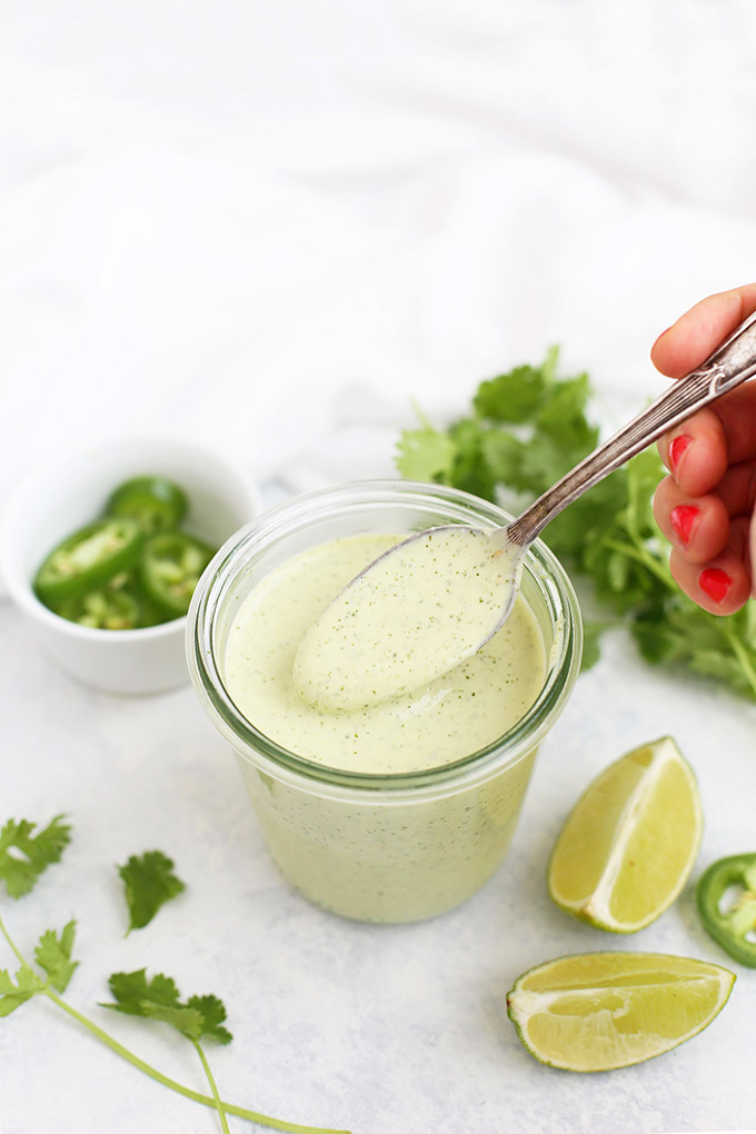 Tomatillo Ranch Dressing in a jar with a spoon. Jalapeño, lime, and cilantro garnish. 