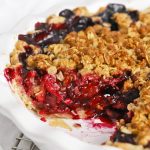 Side view into a triple berry crumble pie, highlighting the bright berry filling and golden crumble topping