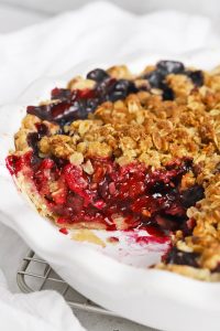 Side view into a triple berry crumble pie, highlighting the bright berry filling and golden crumble topping