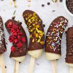 Close-up view of Frozen Chocolate Covered Bananas with different toppings on a piece of parchment paper