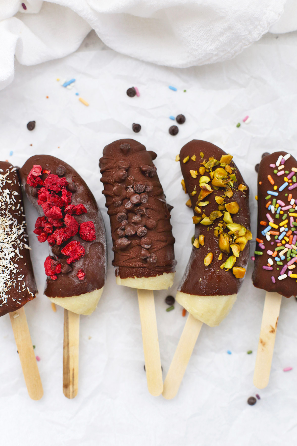 Frozen Chocolate Covered Bananas with different toppings on a piece of parchment paper