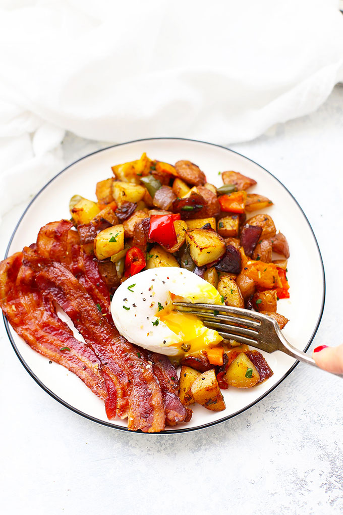 Roasted breakfast potatoes and veggies plated with a soft-poached egg and crispy bacon.