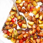 Sheet pan of roasted breakfast potatoes and veggies with a spoon taking a scoop
