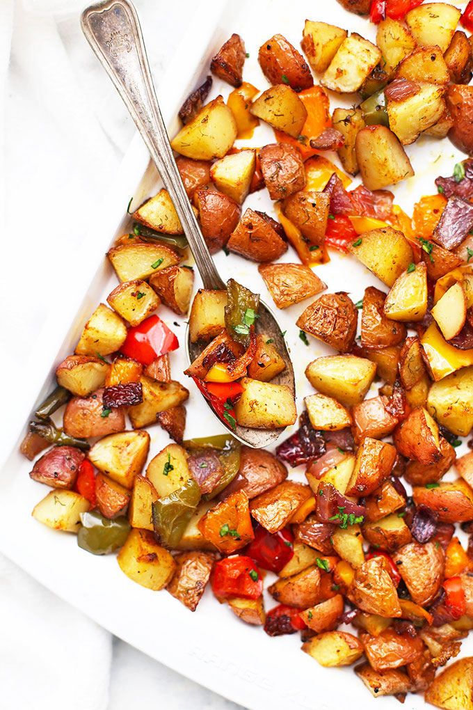 Sheet pan of roasted breakfast potatoes and veggies with a spoon taking a scoop 