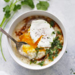 A bowl of congee with a poached egg, tamari, and cilantro