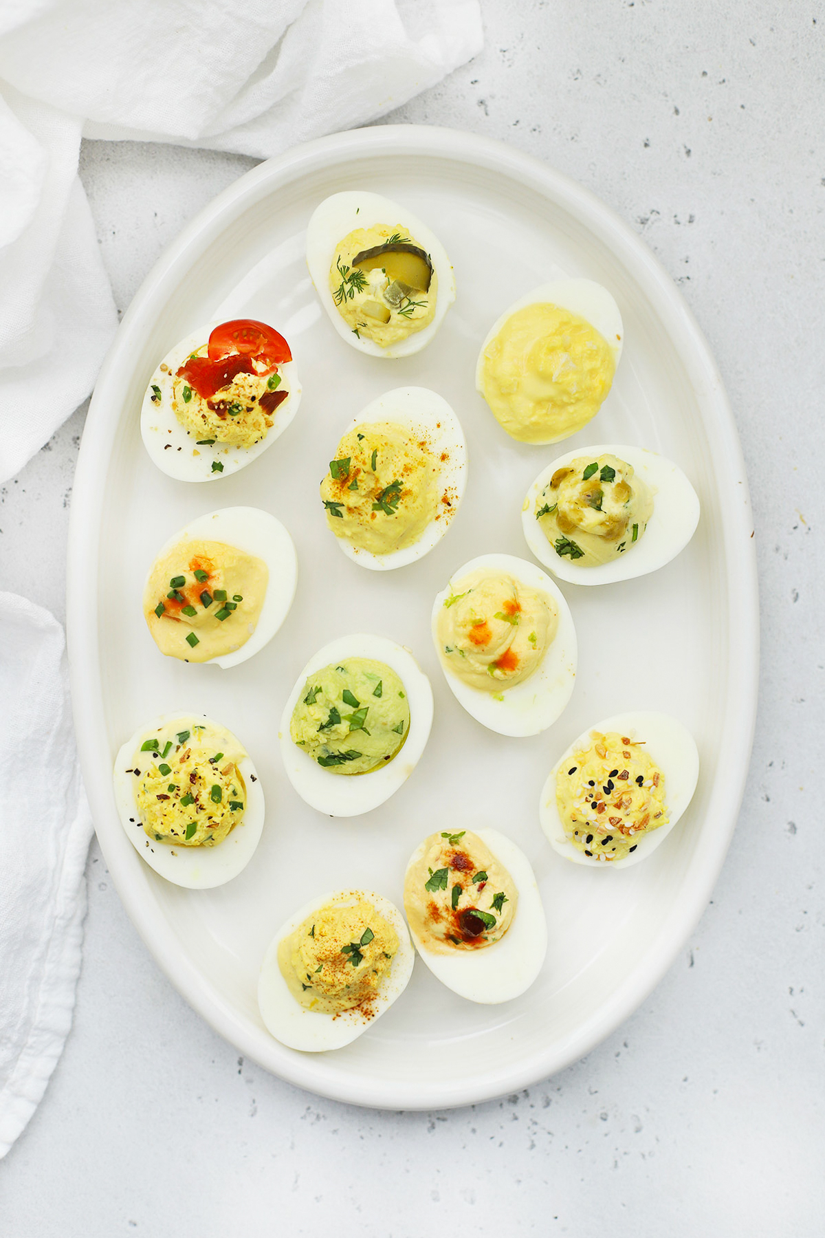 Overhead view of 12 different flavors of deviled eggs on a white platter 