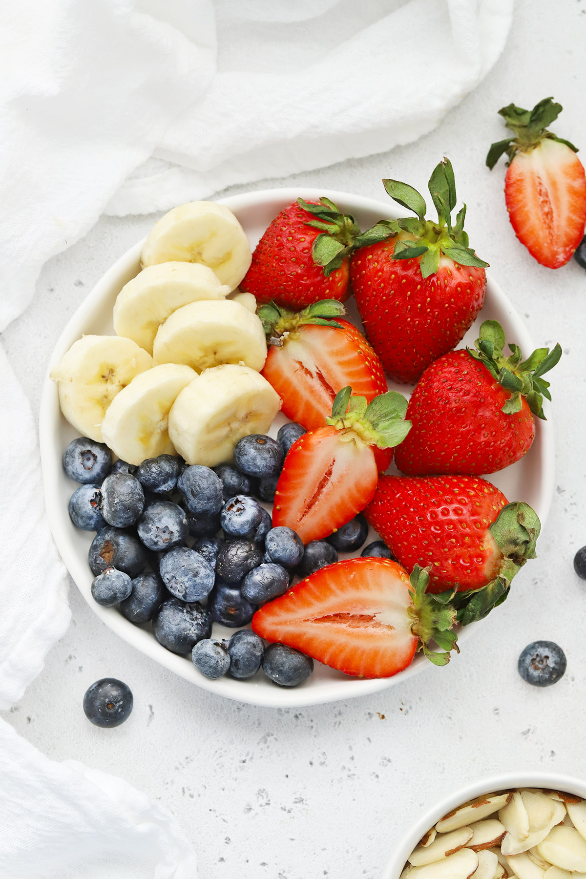 Overhead view of fresh berries and sliced bananas on a plate with a white background
