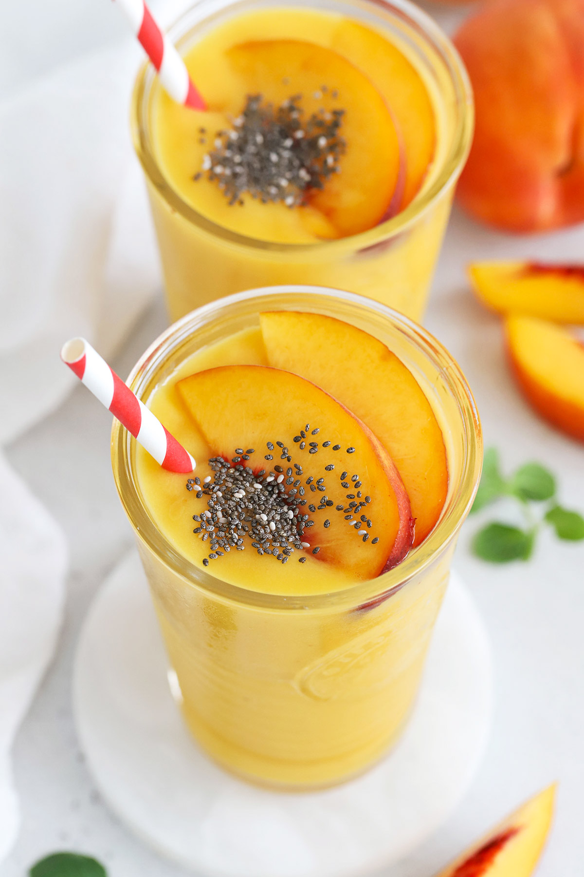 front view of peach mango smoothies topped with fresh peach slices and chia seeds