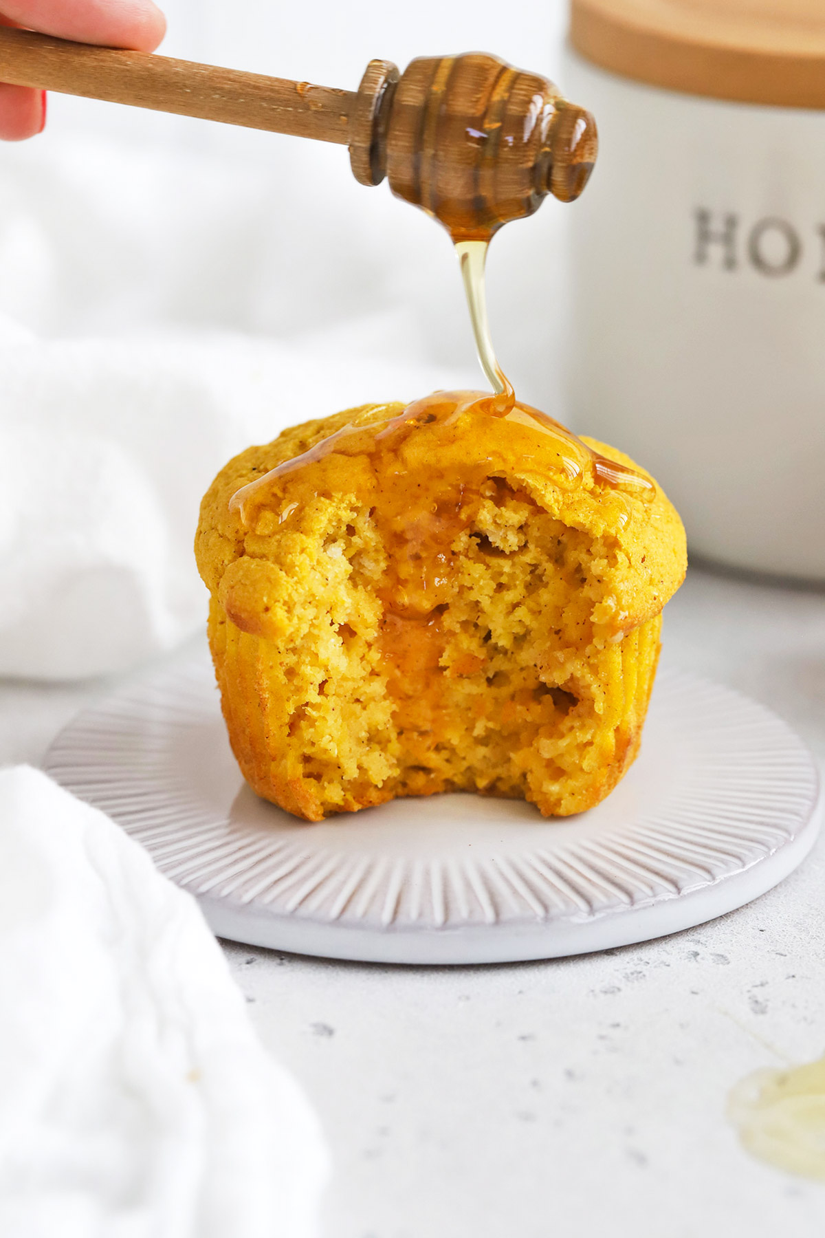 Front view of a gluten-free pumpkin muffin with a bite out of it, being drizzled with honey