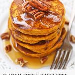 front view of pumpkin pancakes drizzled with maple syrup and toasted pecans
