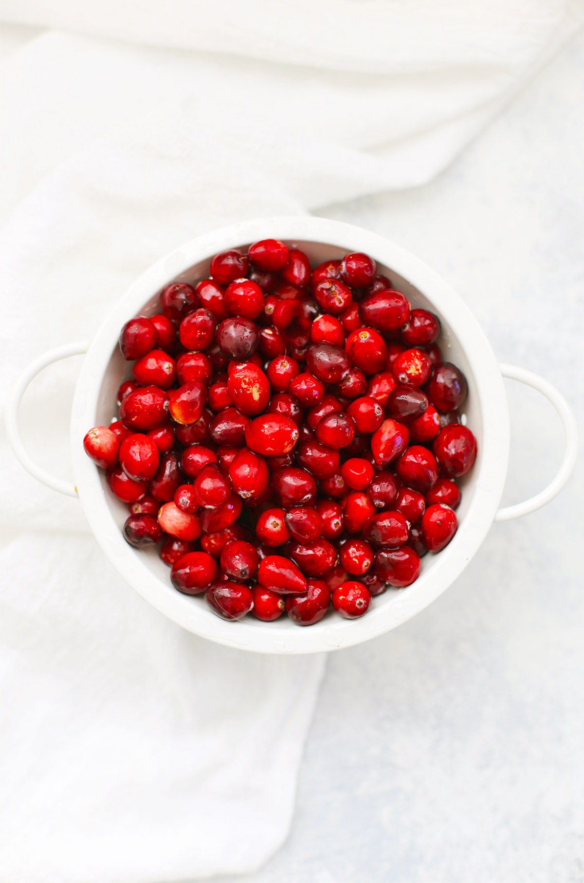 Overhead view of a white colander full of fresh cranberries
