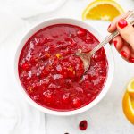 Overhead view of a spoon dipped into a white bowl of naturally sweetened orange honey cranberry sauce
