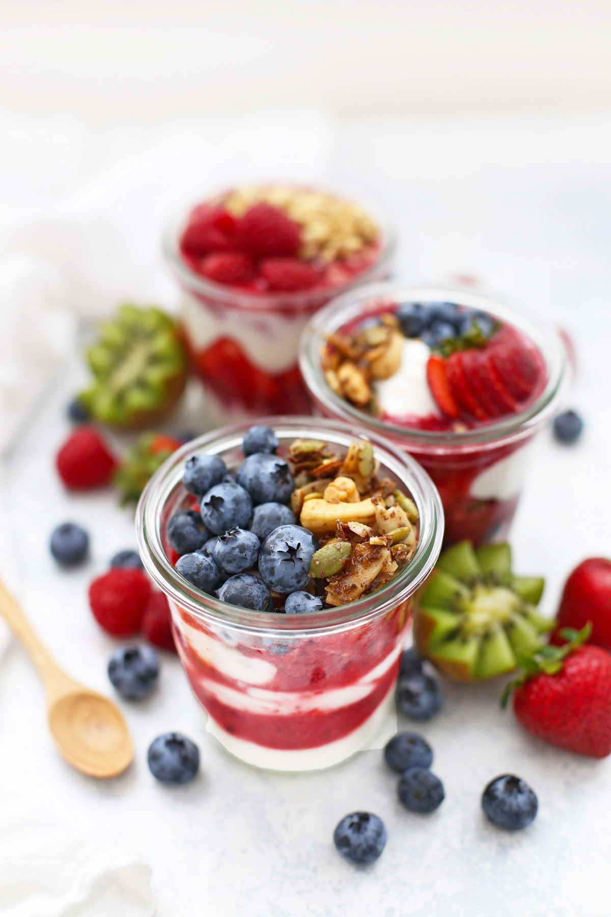 Front View of Jars of Paleo Granola Fruit and Yogurt Parfaits with fresh fruit scattered around the background.