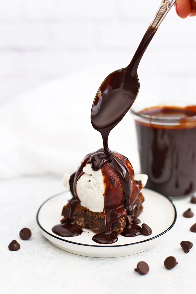 Vegan Hot Fudge Sauce being drizzled over a gluten-free brownie topped with dairy-free vanilla ice cream