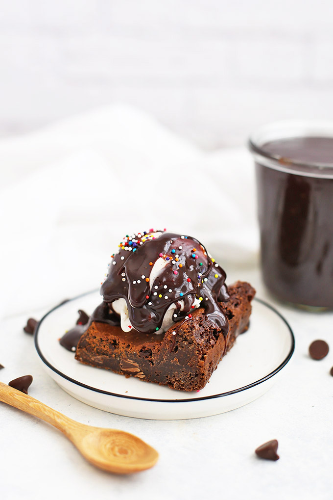 Vegan Hot Fudge Sauce drizzled over a gluten-free brownie with dairy-free ice cream and sprinkles.