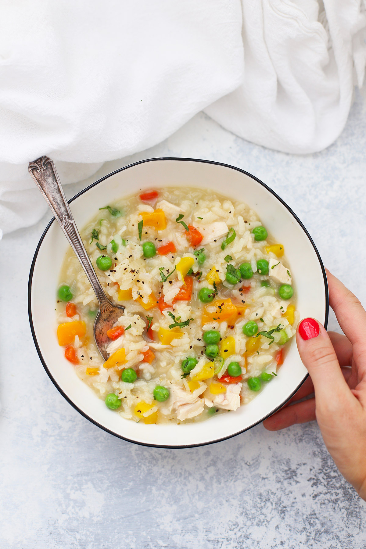 hand setting down a bowl of dairy-free chicken vegetable risotto
