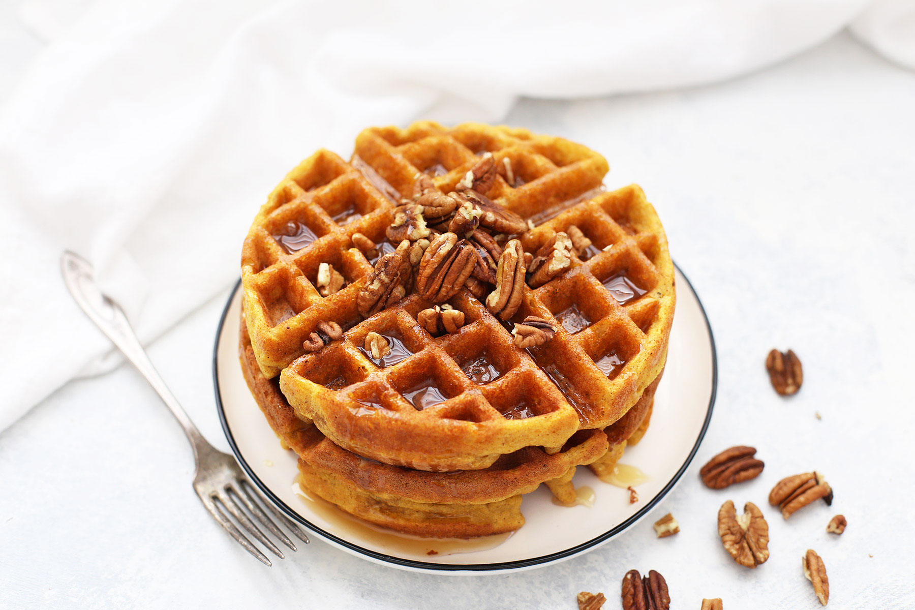 Stack of Almond Flour Pumpkin Waffles with pecans and maple syrup.