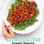Top view of a hand holding a plate of green beans with balsamic pepper relish with text overlay that reads "Paleo + Vegan + Whole30 Green Beans with Balsamic Pepper Relish"