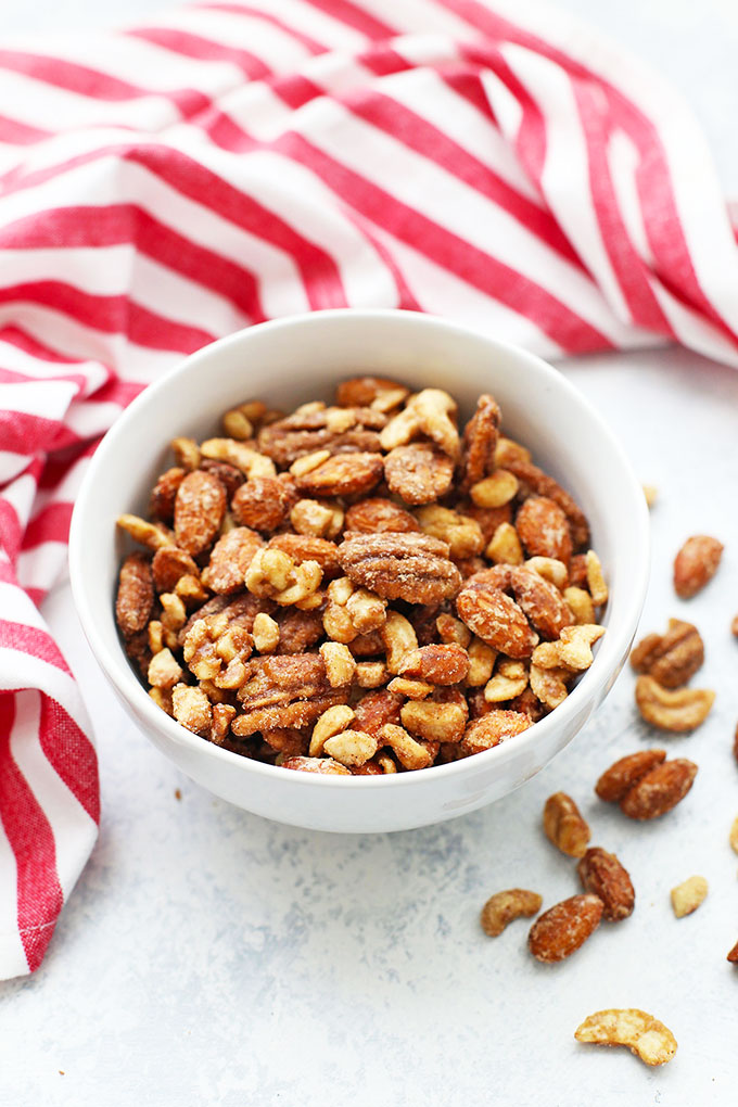 Front view of a bowl of spiced candied nuts with red and white striped dishtowel in the background. 