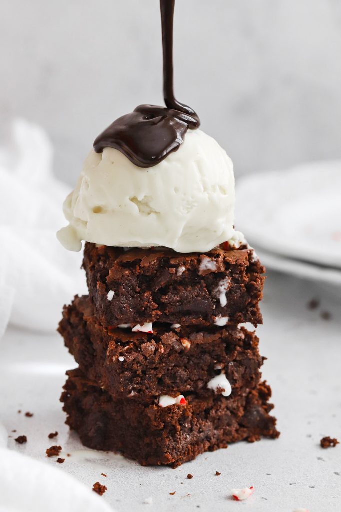 Front view of gluten-free peppermint brownies stacked in a column being topped with vanilla ice cream and drizzled with hot fudge sauce