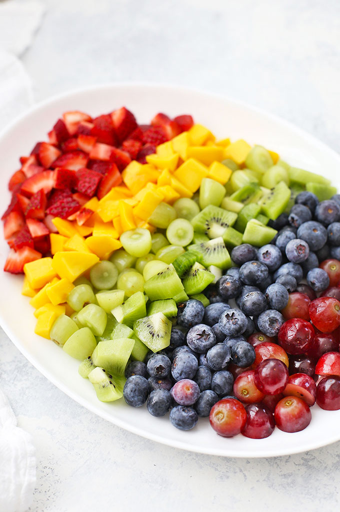 Platter of fruit arranged in rainbow order for Rainbow Fruit Salad with Citrus Mint Dressing from One Lovely Life
