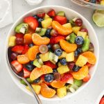 Three bowls of rainbow fruit salad on a white background with lime wedges