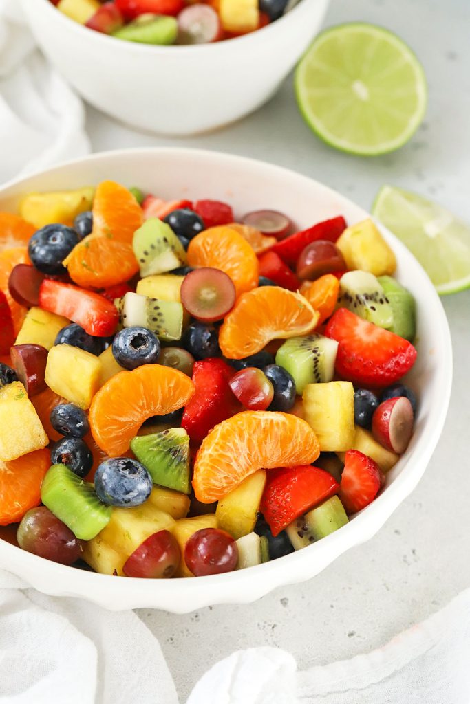 A bowl of rainbow fruit salad with lime wedges in the background