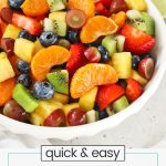 White serving bowl of rainbow fruit salad with honey lime dressing
