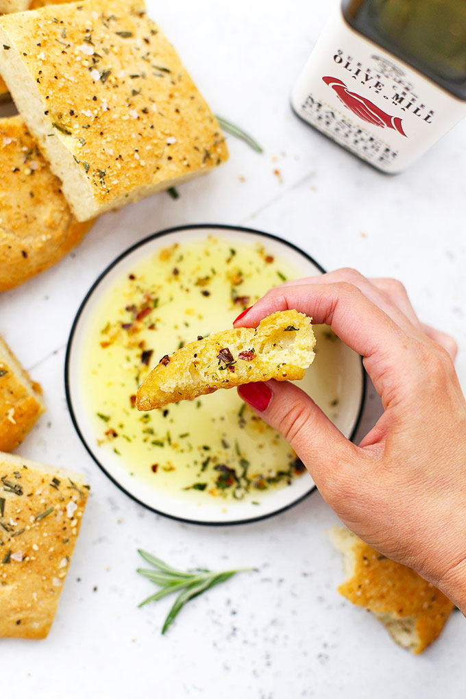 A piece of gluten free focaccia dipped into olive oil and herbs