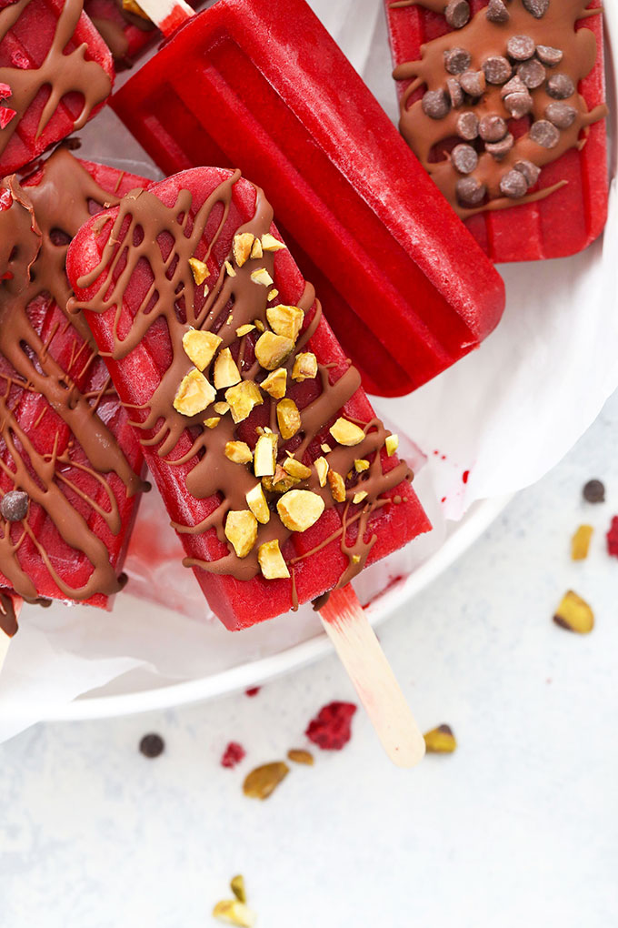 Close up view of a Healthy Raspberry Sorbet Popsicle topped with vegan magic shell and chopped pistachios