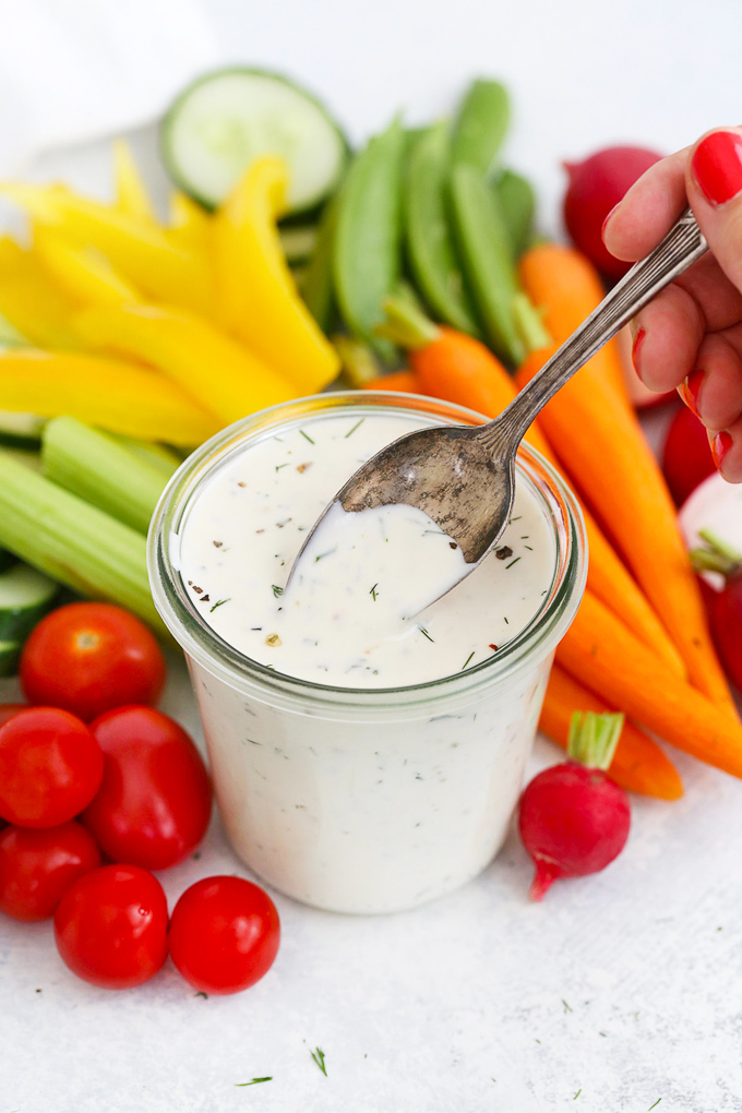 Spoon scooping dairy free paleo ranch dressing with fresh veggies in the background