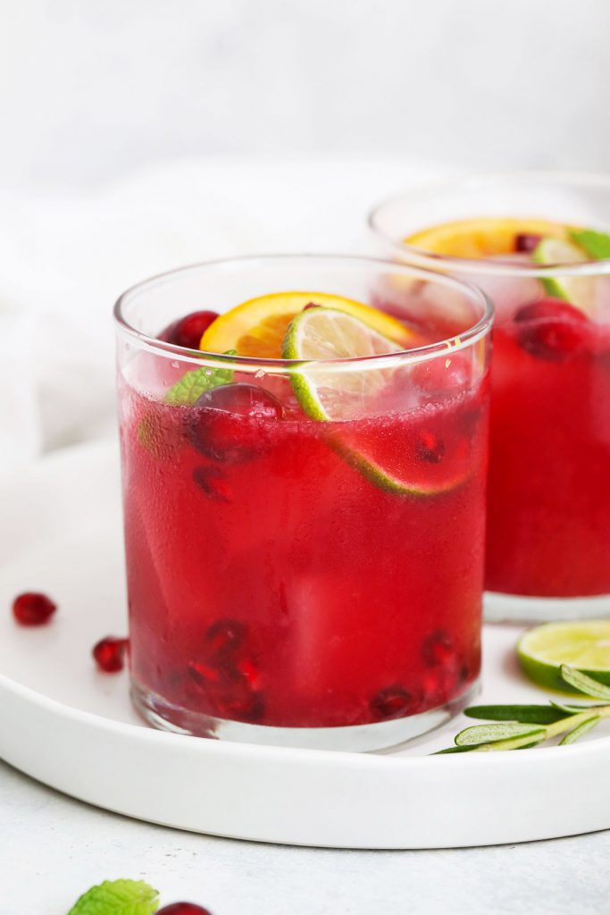 Front view of Two Non-alcoholic sparkling citrus pomegranate mocktails on a white plate