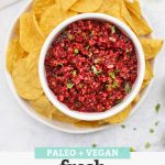 Overhead view of a bowl of fresh cranberry salsa with tortilla chips with text overlay that reads "Paleo + Vegan Fresh Cranberry Salsa: A Fun Holiday Appetizer!"