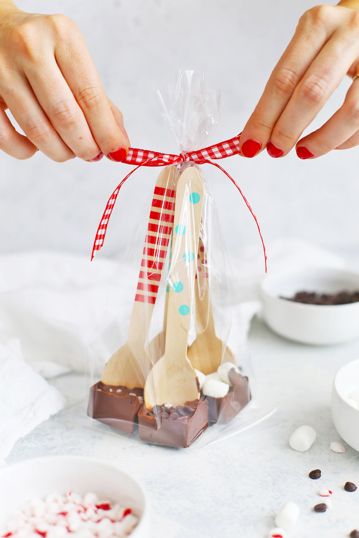 Four hot chocolate spoons wrapped in a clear treat bag being tied with red ribbon