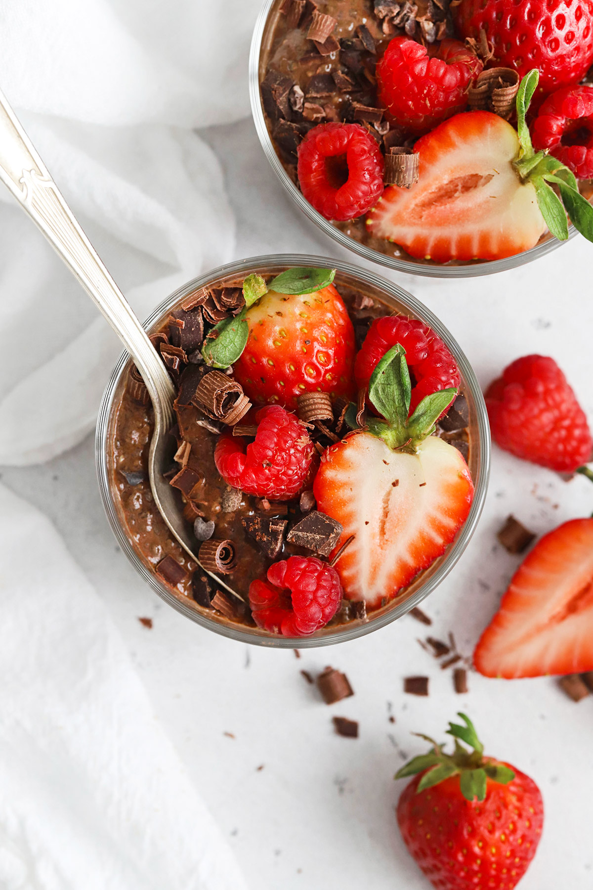 Overhead view of two bowls of chocolate chia pudding topped with fresh berries and shaved chocolate