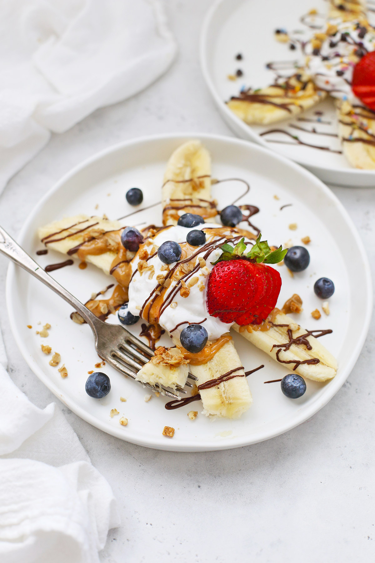Front view of Healthy Banana Split with Yogurt, Peanut Butter, Chocolate, and berries on a white plate