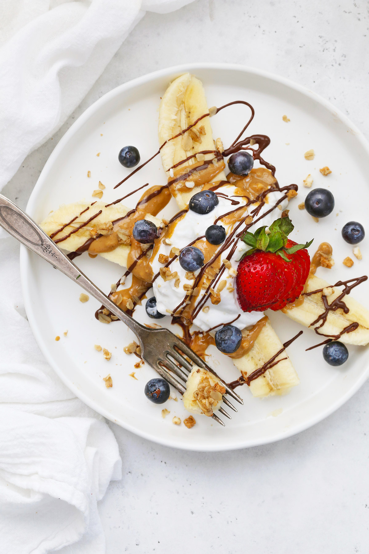 Close view of Healthy Banana Split with Yogurt, Peanut Butter, Chocolate, and berries on a white plate