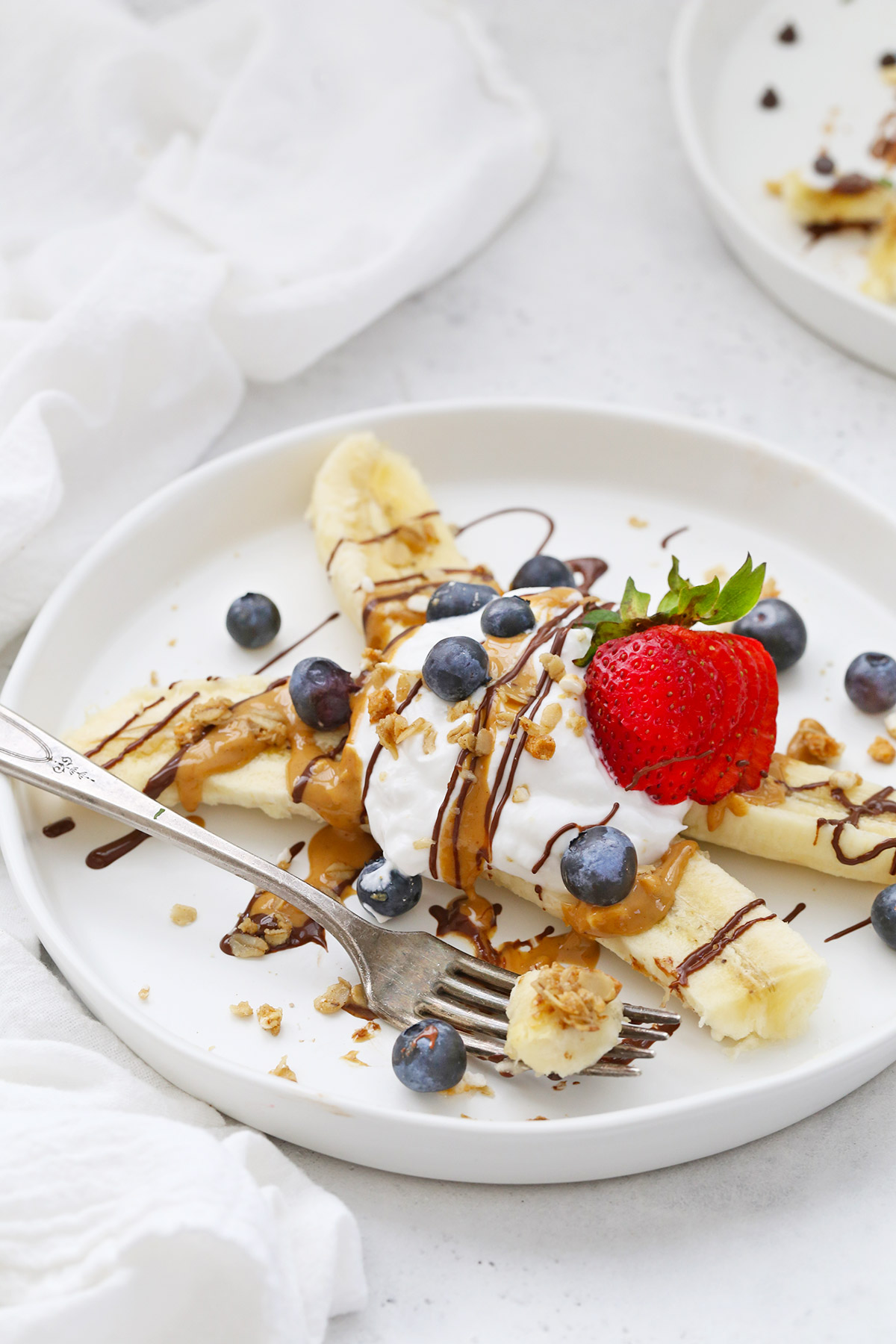 Close-up view of Healthy Banana Split with Yogurt, Peanut Butter, Chocolate, and berries on a white plate