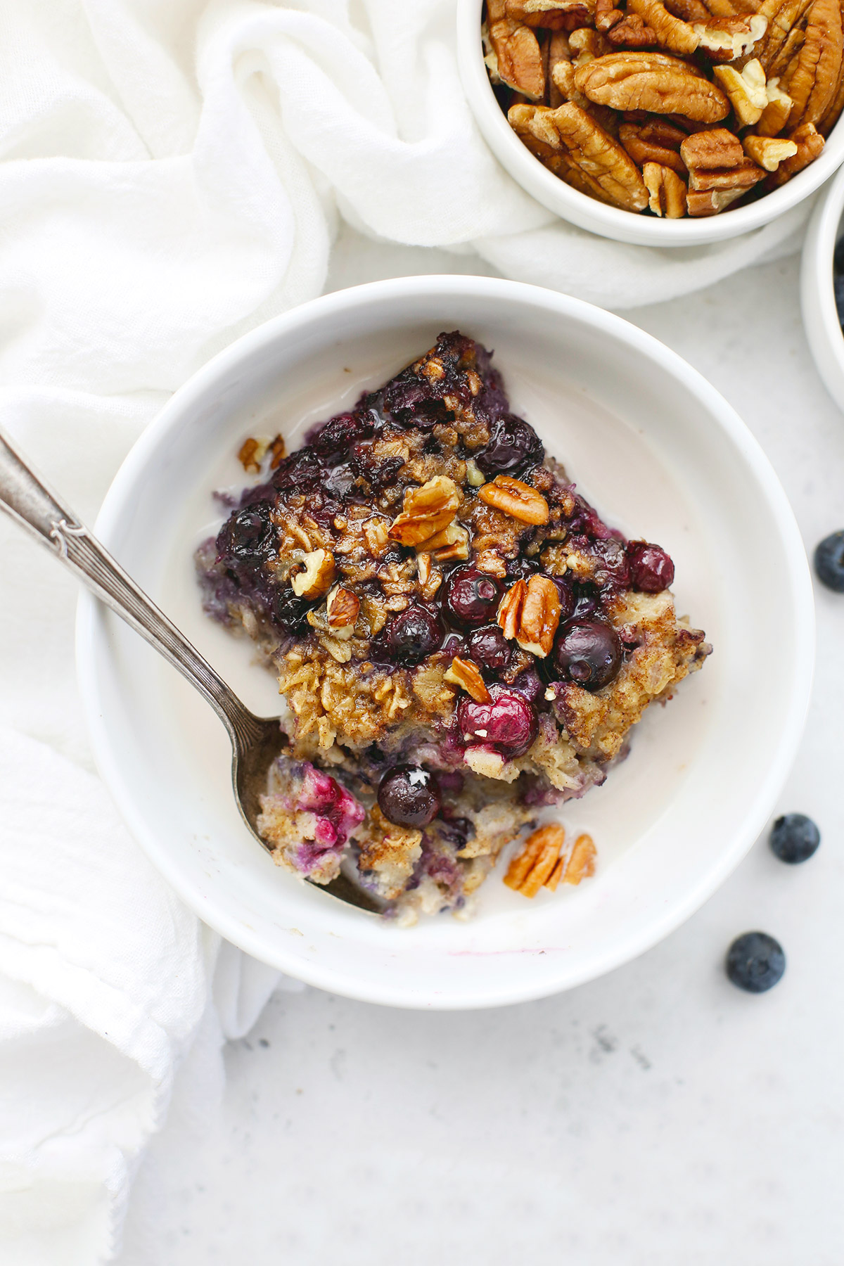Overhead view of a bowl of blueberry baked oatmeal with almond milk on a white background. 