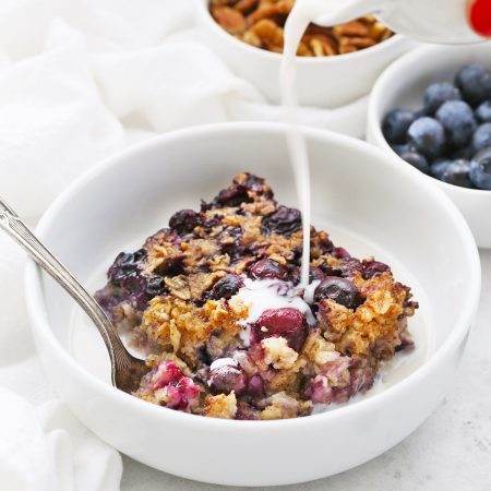 Pouring almond milk over a bowl of blueberry baked oatmeal.